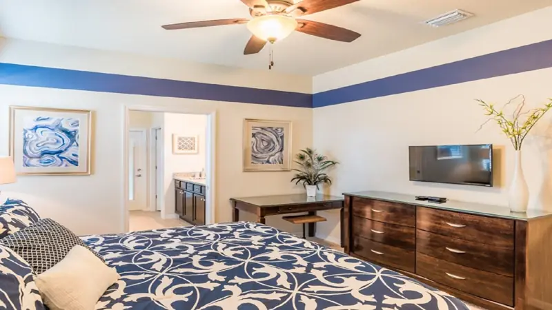 down king stairs master access to pool – A bedroom with a bed, a desk, a dresser, a ceiling fan, and a TV.